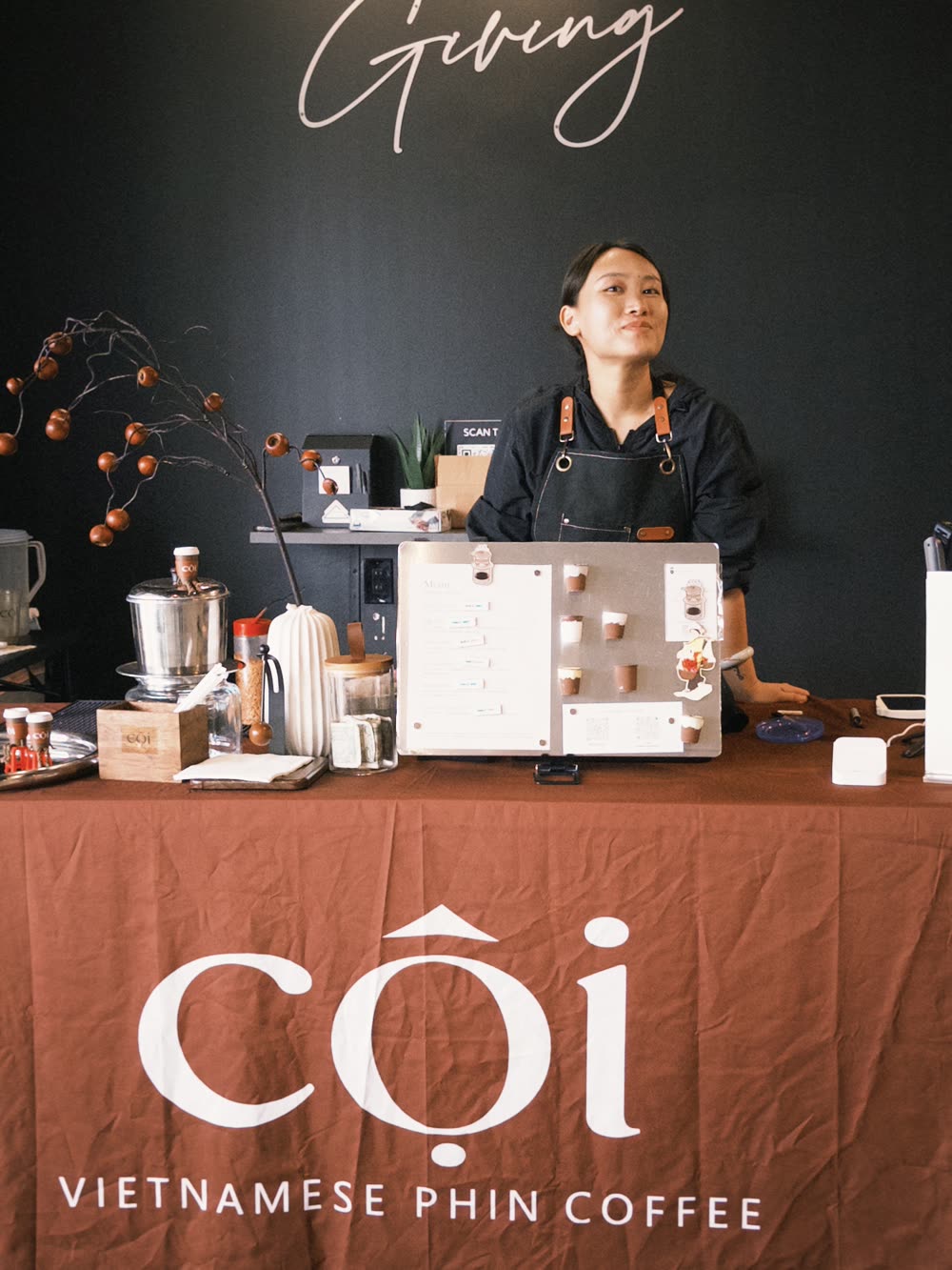 A Cội barista behind the branded pop-up table, phin station and menu set up at an event.