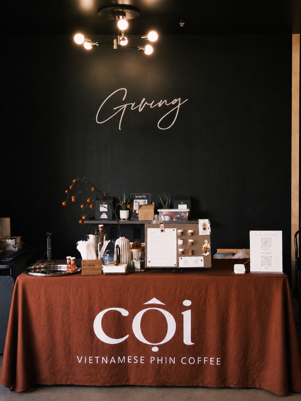 The Cội pop-up stall — a phin coffee setup on a rust linen table with the Cội wordmark.